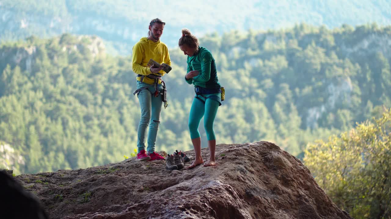 一男一女攀岩者站在岩石悬崖下，看着挑战性的路线，准备攀登。以自然岩石为背景，进行野外活动组合训练视频下载