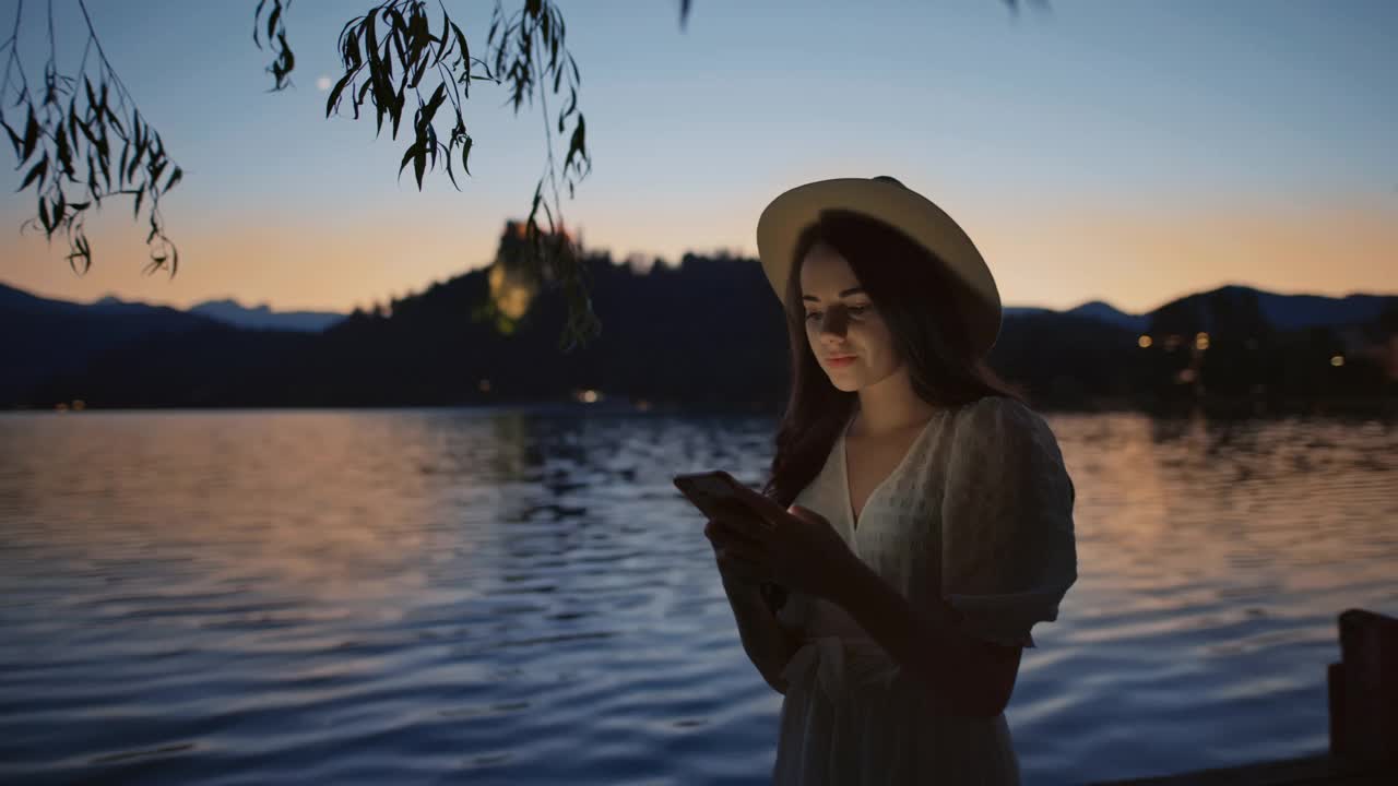 黄昏时分，一名年轻女子在布莱德湖使用智能手机视频下载
