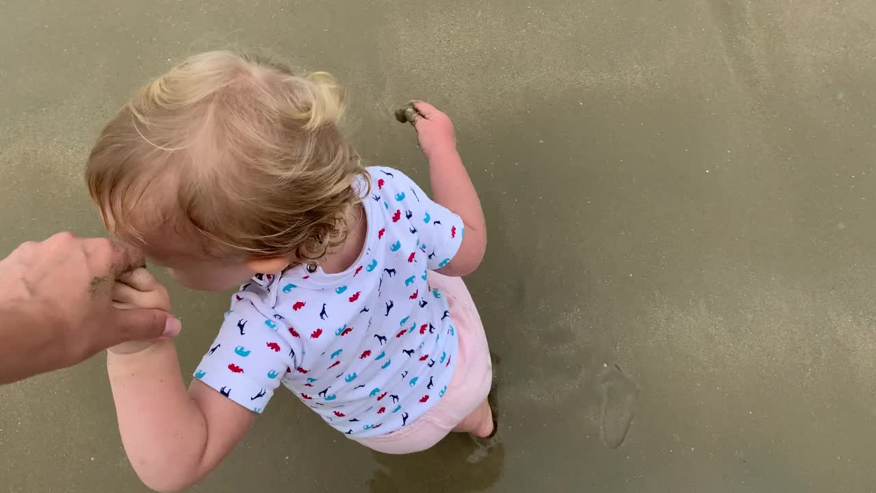 微笑的蹒跚学步的女孩牵着妈妈的手在海滩上散步视频素材