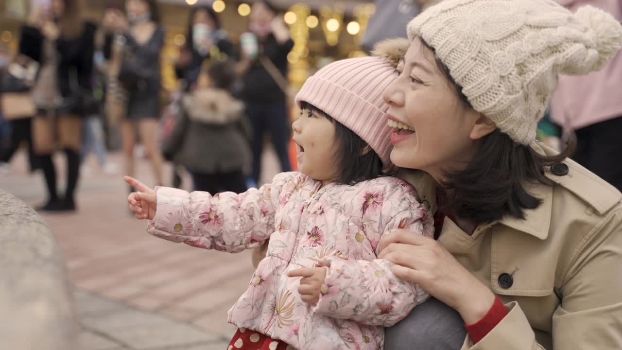 中国台湾的母亲和婴儿笑着看着城市广场上跳舞的喷泉，以一群游客为背景拍照视频下载