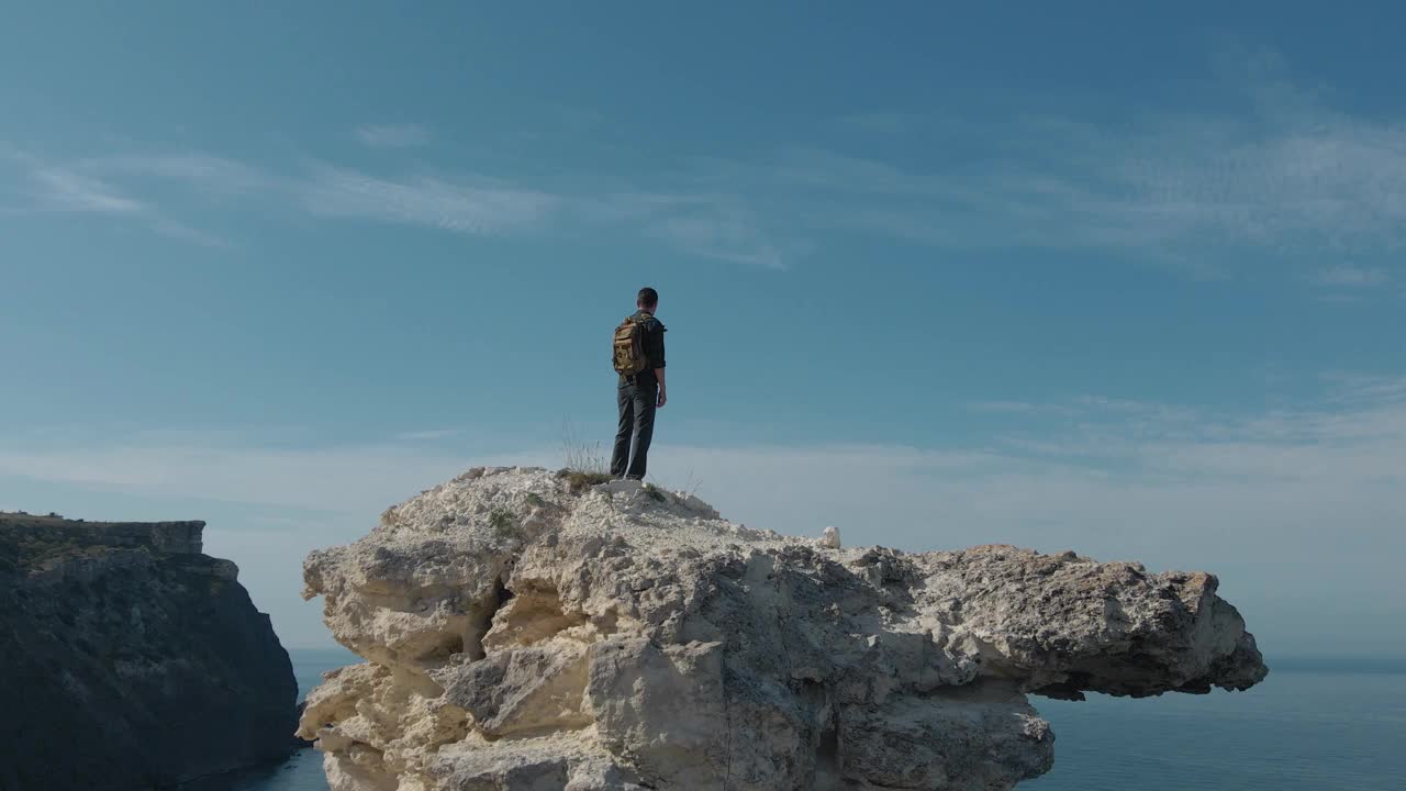 缓慢的空中旋转无人机视图主动徒步旅行的人与背包站在岩石山附近的蓝色的海与天空地平线在户外休闲娱乐旅游活动冥想灵感视频下载