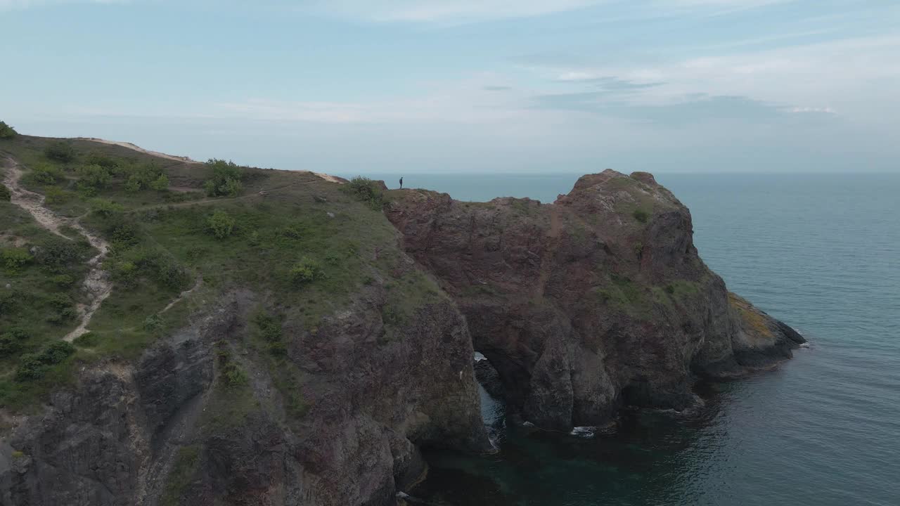 在户外休闲、娱乐、体育活动期间，主动徒步旅行的男性人类与背包沿着岩石山与天际线附近的蓝色海洋视频下载