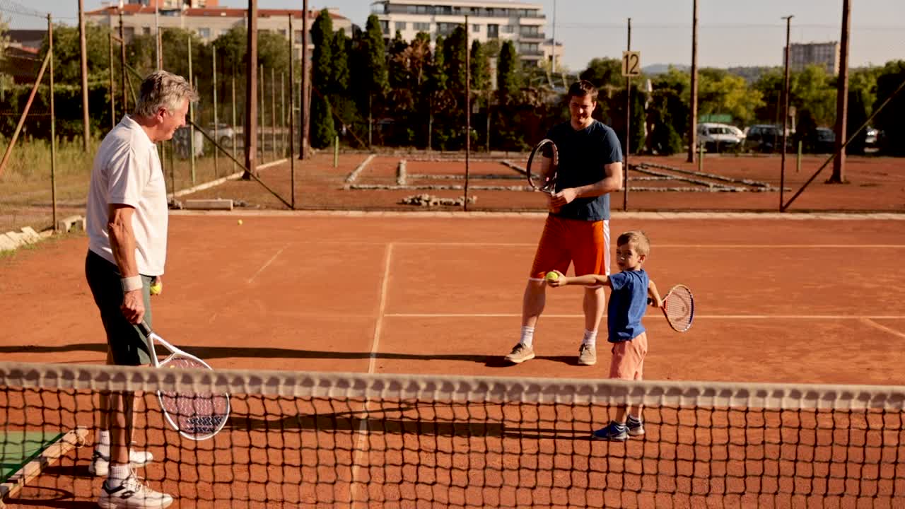 可爱的小男孩，在父亲和祖父的帮助下学会了打网球视频下载