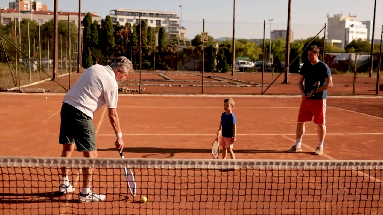 慈爱的父亲和祖父，学习好奇和可爱的男孩如何打网球视频下载