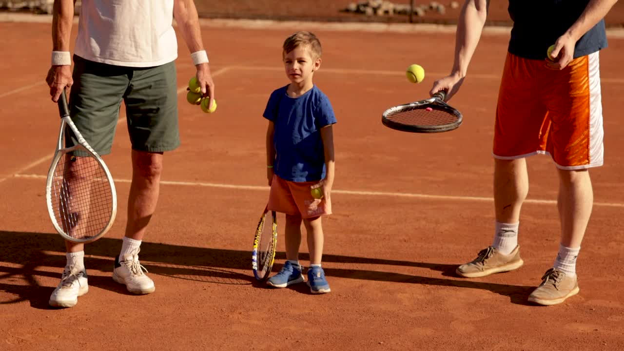 可爱的男孩享受家庭时光，与他的爷爷和父亲在网球练习视频下载