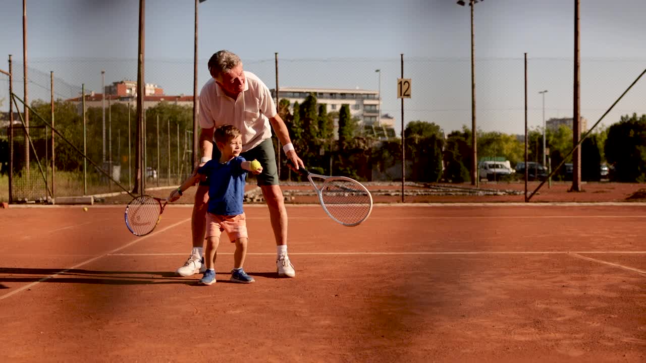 在网球练习期间，骄傲的爷爷和他可爱的孙子击掌庆祝视频下载