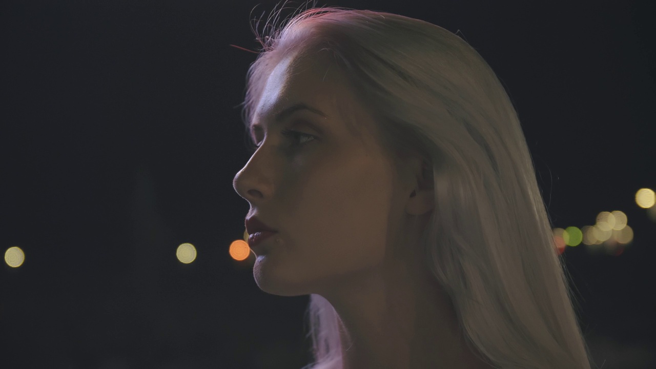一名年轻女子的肖像，背景是夜晚的城市灯光，在她的脸上玩不同的颜色。缓慢的运动。特写镜头。视频下载
