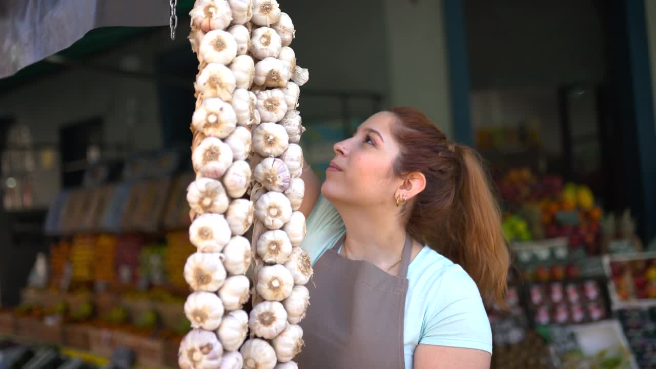 一名拉美妇女在农贸市场的小摊上挂着洋葱辫，对着镜头微笑视频下载