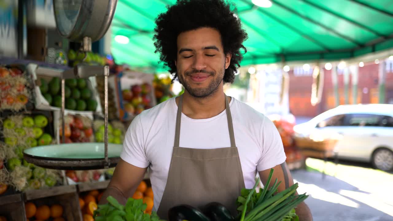 一名黑人男子在果蔬市场工作，手里拿着装满新鲜食物的美味篮子，对着镜头微笑视频下载