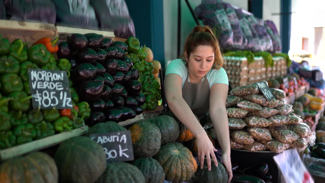 一个年轻的拉丁美洲妇女在农贸市场的摊位上布置南瓜展览视频下载