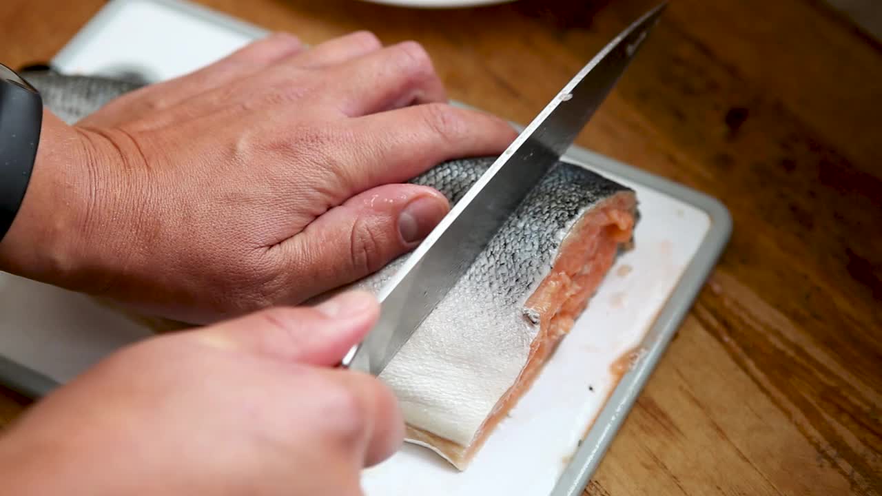 男子在塑料板上切割红色的鱼。厨师在厨房切三文鱼。厨师把鳟鱼切成牛排。手切密友。用锋利的钢刀在砧板上把鲜鱼切成薄片视频下载