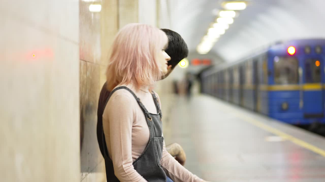 当火车慢动作离开时，一对年轻夫妇坐在地铁站室内。中景:在城市里等待交通工具的白人千禧一代男女。的生活方式。视频素材