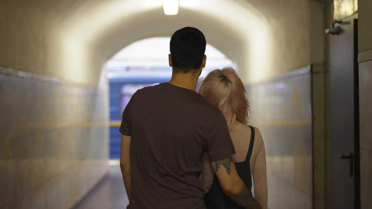 后景:千禧一代夫妇站在室内的大都会月台上拥抱在一起，背景是慢动作的地铁列车。等待公共交通工具的年轻白人男女。视频素材
