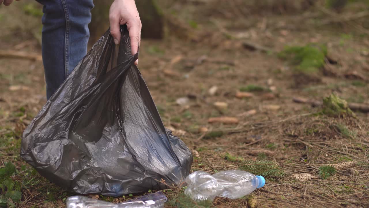 一个男人用黑色的袋子收集塑料垃圾。关闭了。我们从垃圾中拯救大自然。视频素材