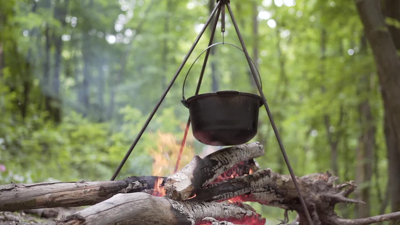 在森林徒步旅行时，圆顶礼帽和美味的粥站在篝火上的三脚架上视频素材