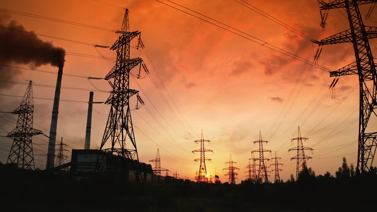 日落时的高压电缆和塔架。电力塔的轮廓映衬着戏剧性的天空和红色的夕阳。视频素材