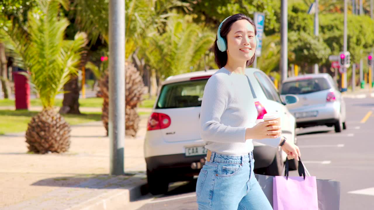 一个美丽的年轻女子戴着耳机，喝着咖啡，在城市购物的4k视频片段视频购买