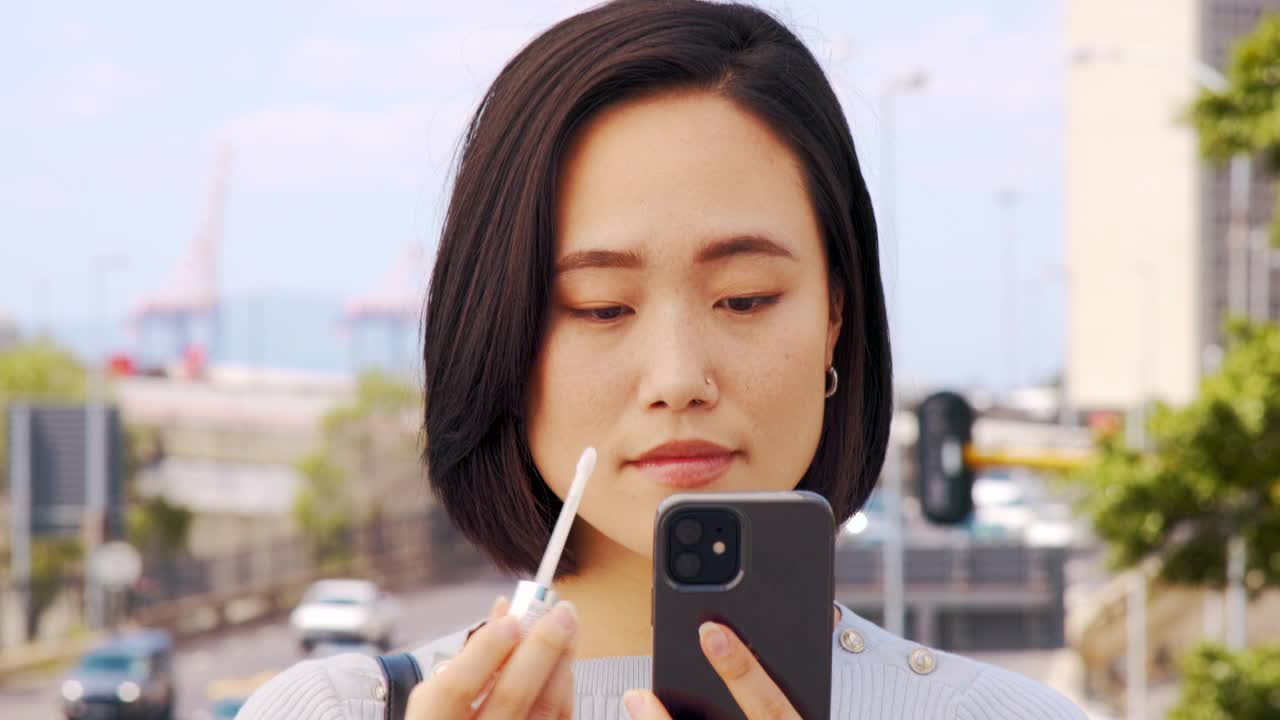 一个美丽的年轻女子在城市外面用手机当镜子涂口红的4k视频片段视频下载