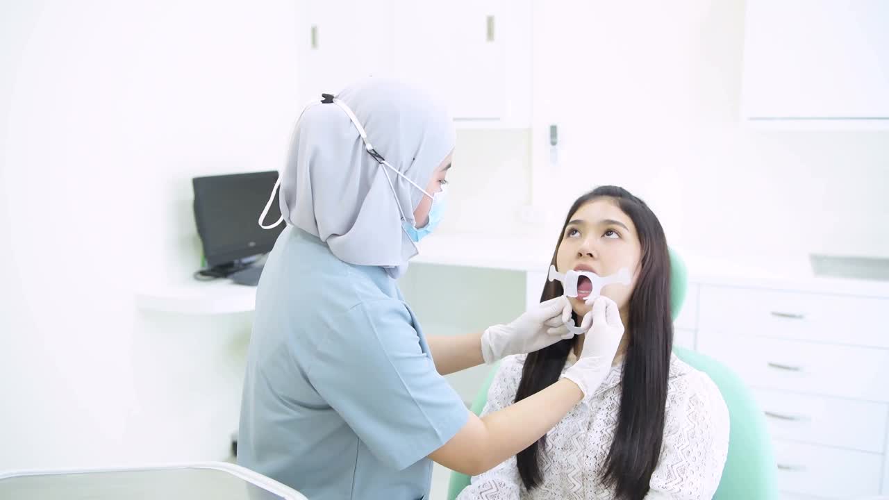 牙医检查年轻妇女的牙齿坐在牙医椅子上视频下载