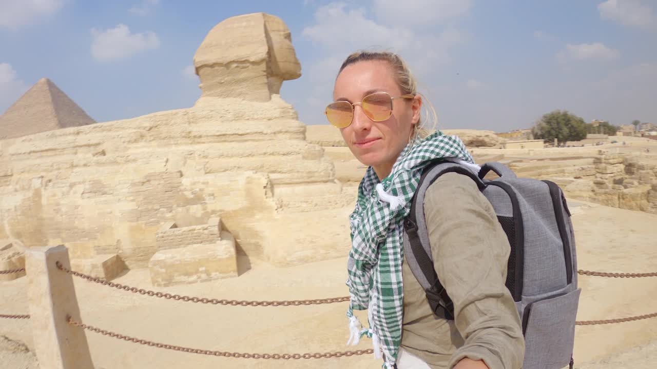 一名年轻女子在埃及开罗的大金字塔上与狮身人面像自拍。一名女子在埃及观光时自拍视频下载