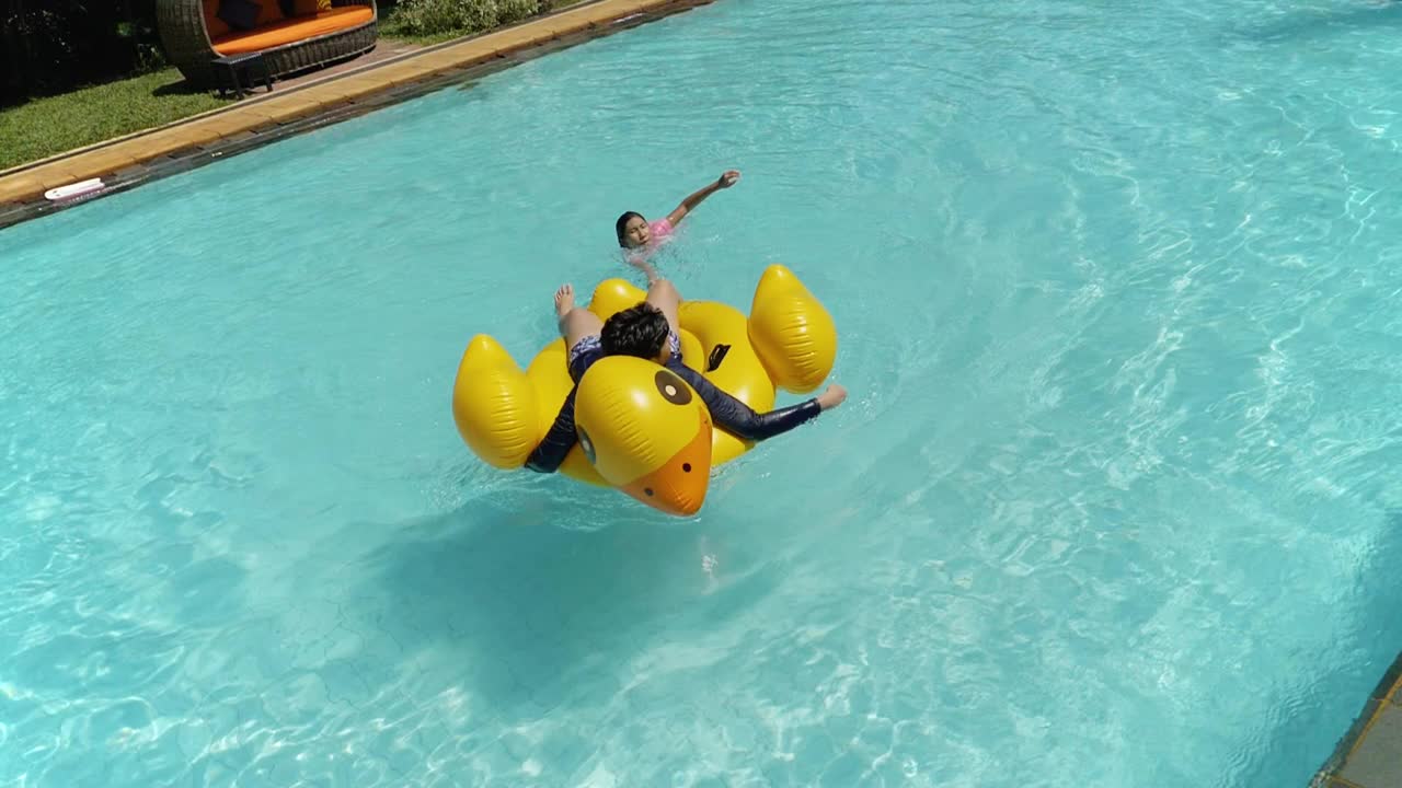快乐的亚洲儿童在度假期间与家人在酒店或度假胜地一起在泳池中玩黄鸭橡皮艇，生活理念。视频素材