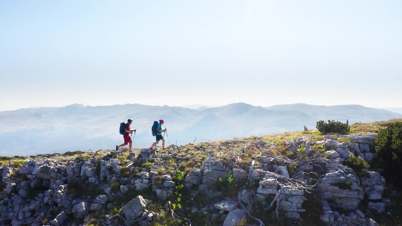 在阳光明媚的夏日，两个人带着登山杆和背包沿着岩石山上山，在克罗地亚旅游视频下载