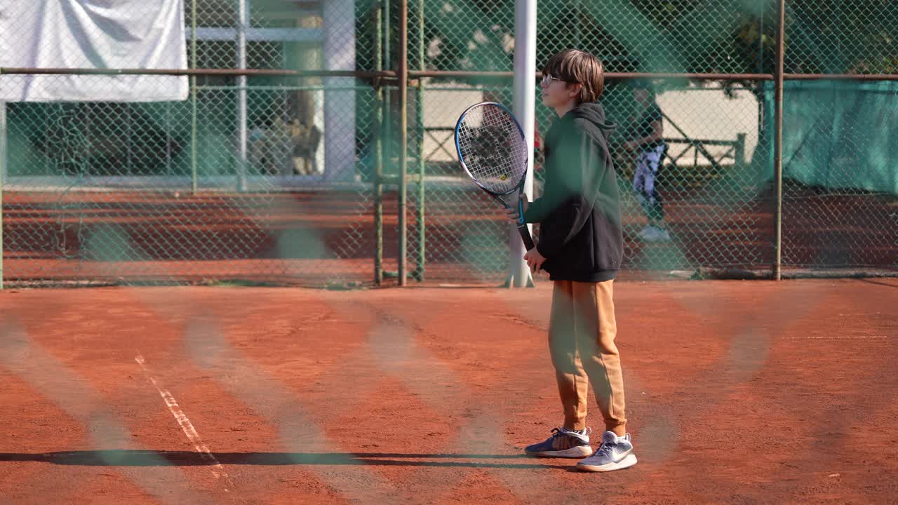 男孩在室外红土球场打网球。视频下载