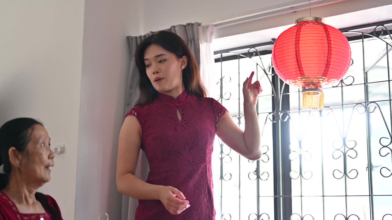 年轻的亚洲孙女帮助她的祖母准备挂新的红色的中国灯笼视频素材