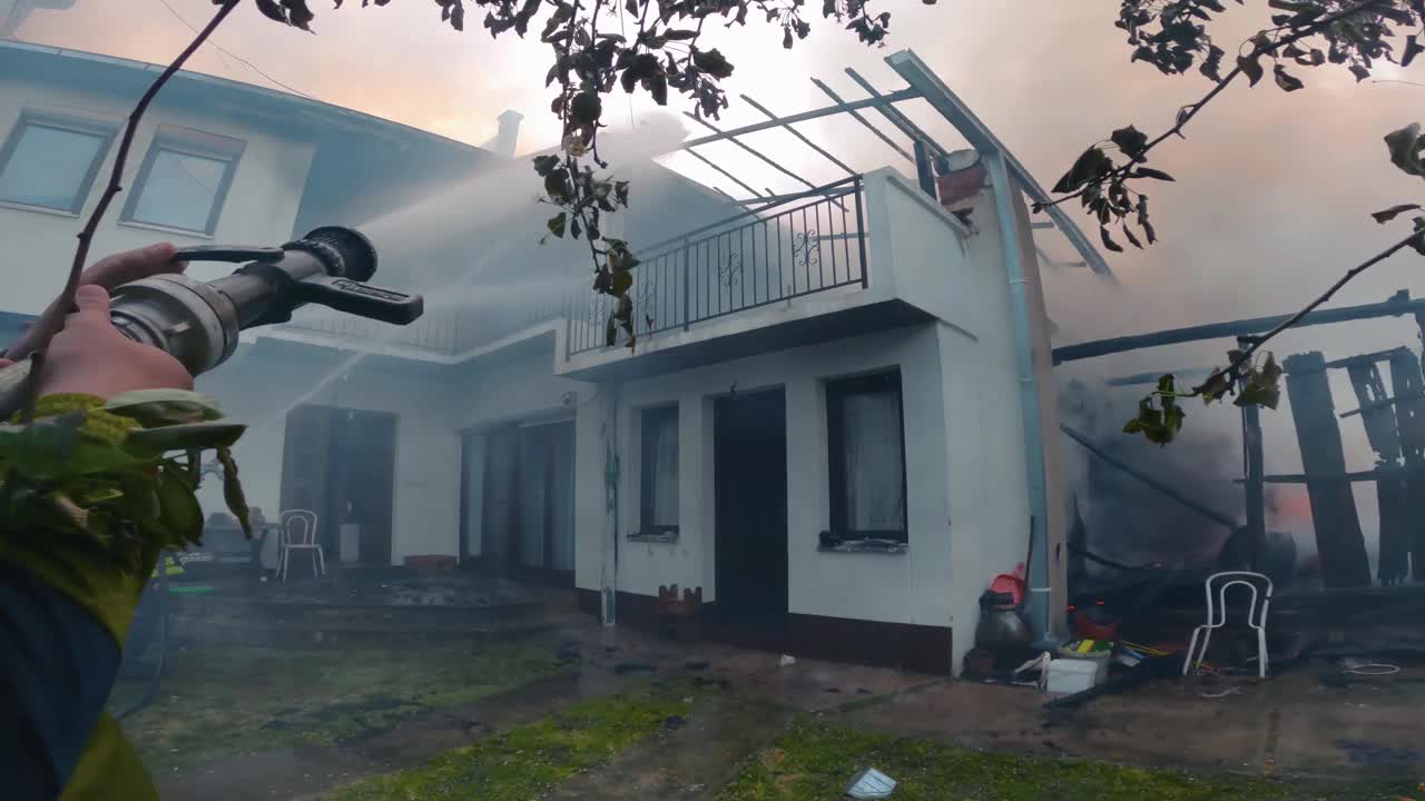 消防队员从消防水管中喷水，扑灭了燃烧着的房子里的大火视频素材