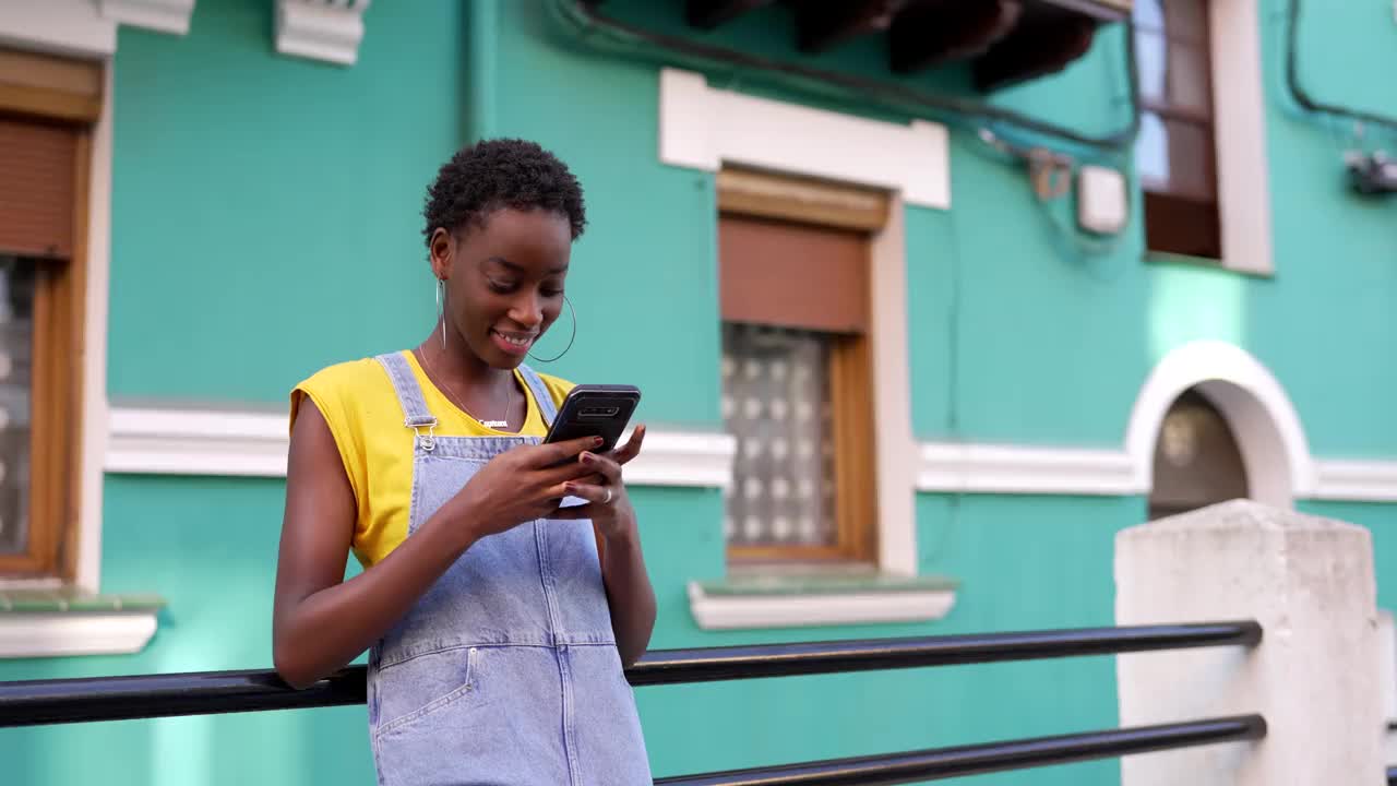非裔美国妇女对着绿松石色的墙壁使用手机视频下载
