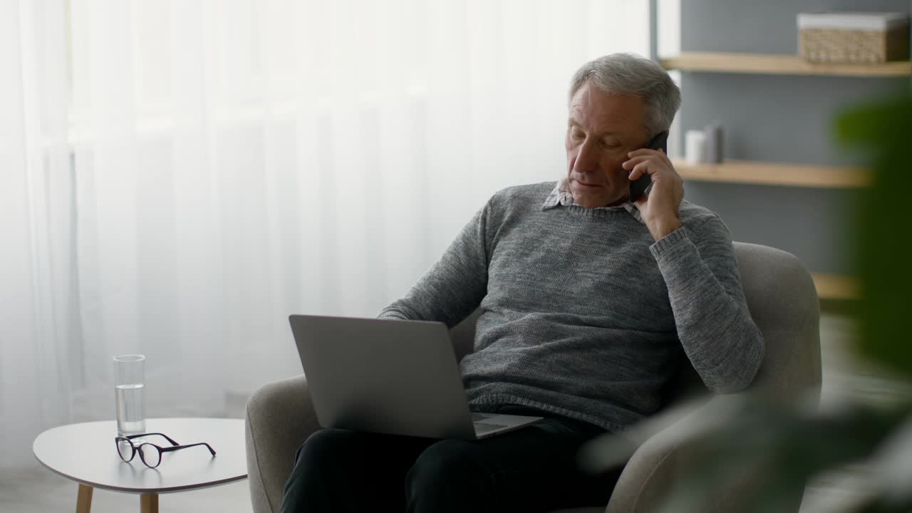 退休自由职业。老年人在家使用手机和笔记本电脑视频素材