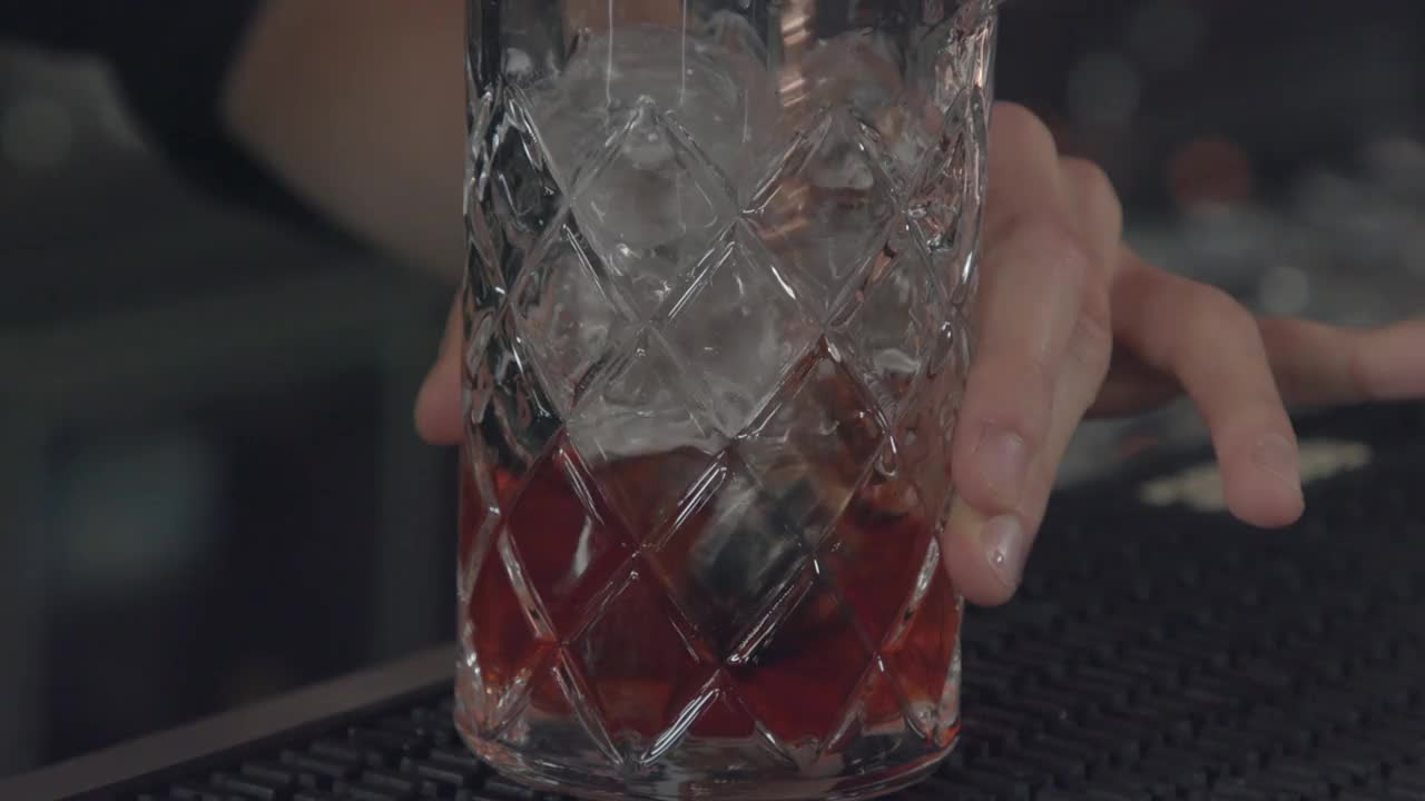 调酒师在酒杯中搅拌加冰的红色鸡尾酒视频下载