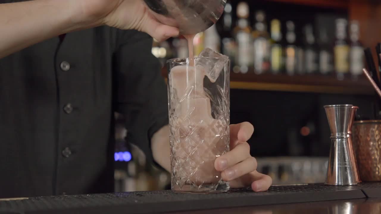 调酒师将桃色鸡尾酒从摇酒器倒入盛满冰块的玻璃杯中视频下载