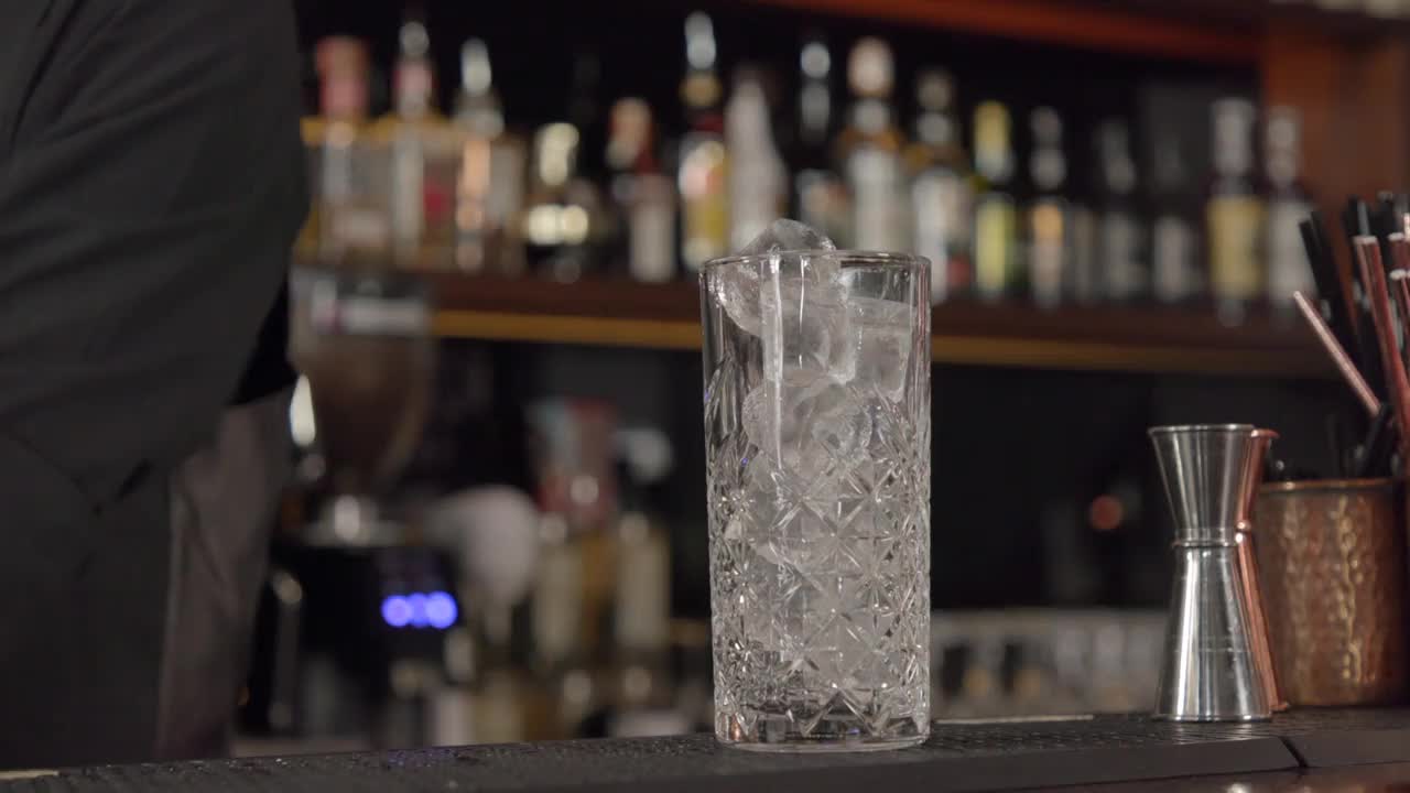 调酒师将蜜桃色的鸡尾酒从摇酒器倒入盛满冰块的玻璃杯中视频下载