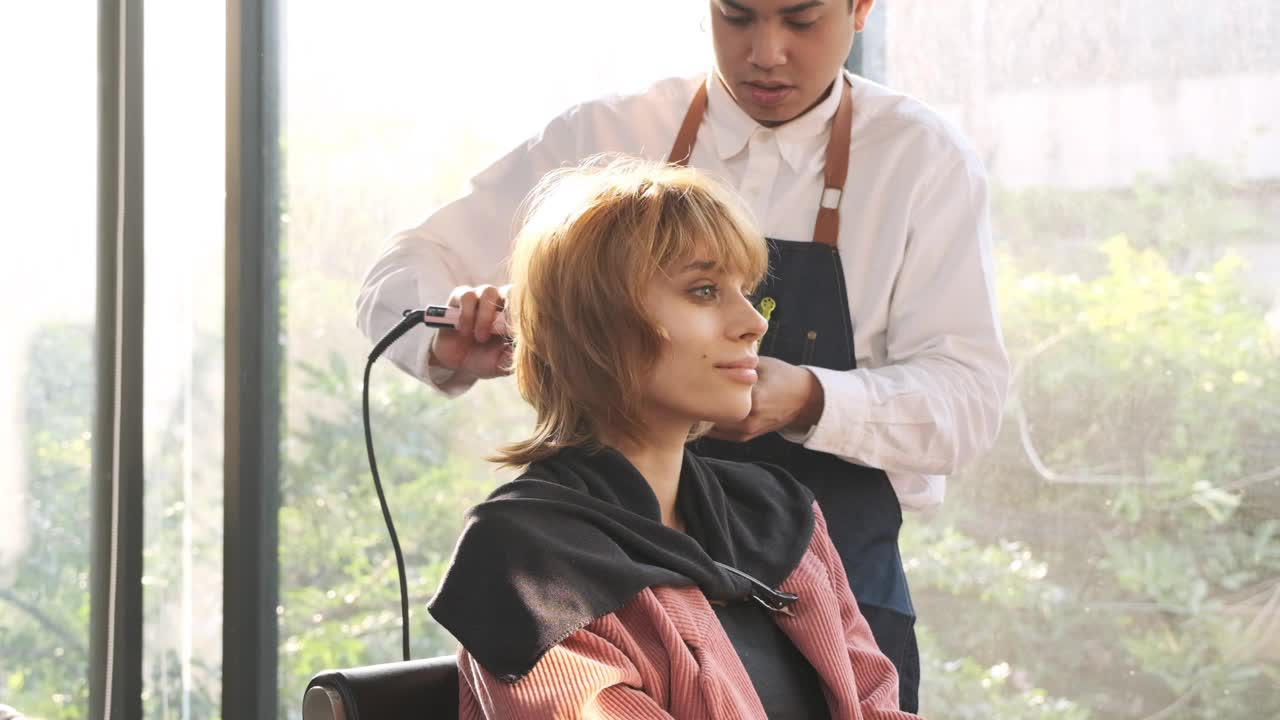 美发师在美容院用小吹风机为漂亮的白人女性做头发。视频下载
