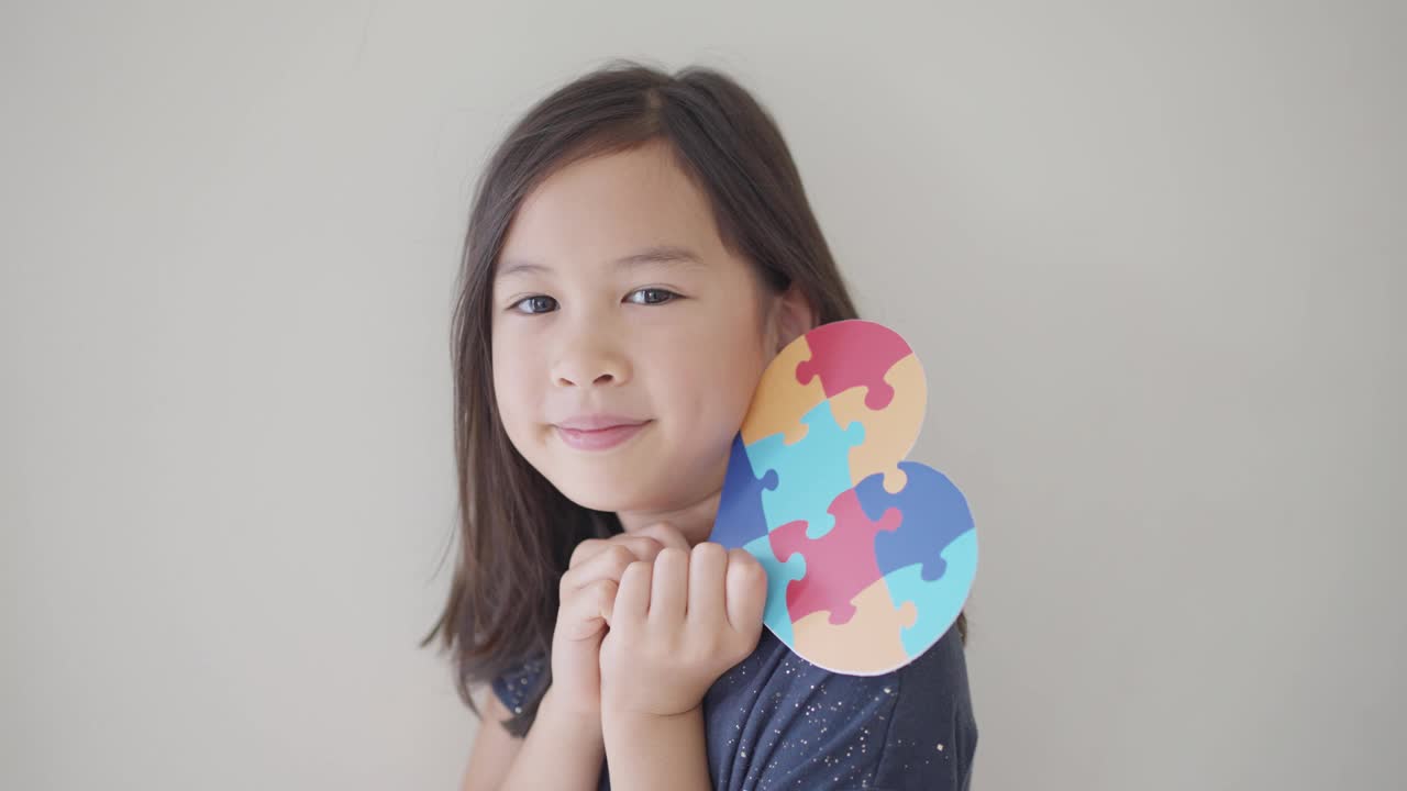 亚洲混血女孩手里拿着拼图心形拼图，学龄前儿童心理健康概念，世界自闭症意识日，自闭症谱系障碍意识概念视频素材