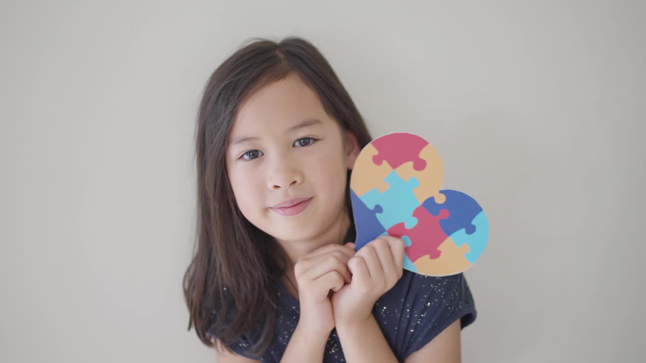 亚洲混血女孩手里拿着拼图心形拼图，学龄前儿童心理健康概念，世界自闭症意识日，自闭症谱系障碍意识概念视频素材