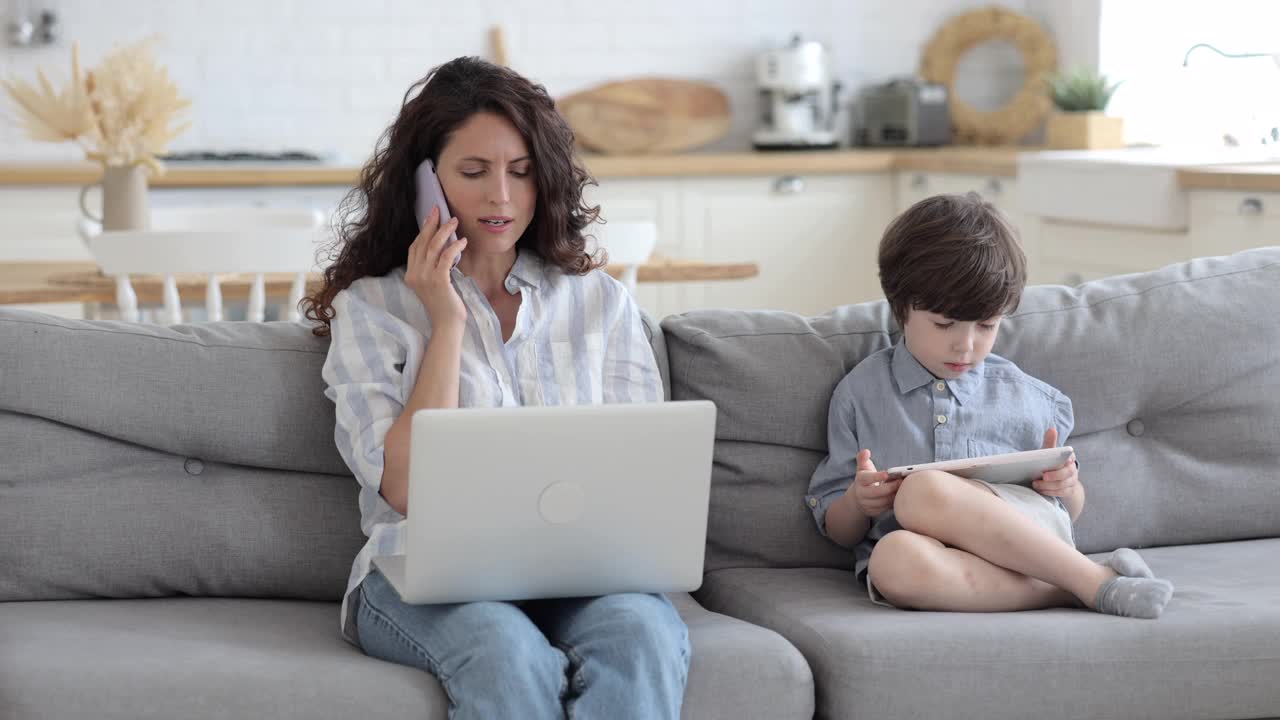 女企业家妈妈打电话，坐在沙发上和儿子一起玩平板电脑游戏视频素材