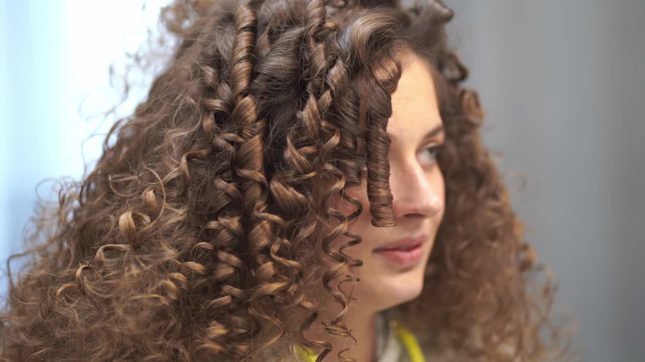 一个年轻的卷发女人正在做头发的特写，她笑着看着镜头，把她的头转向不同的方向视频下载