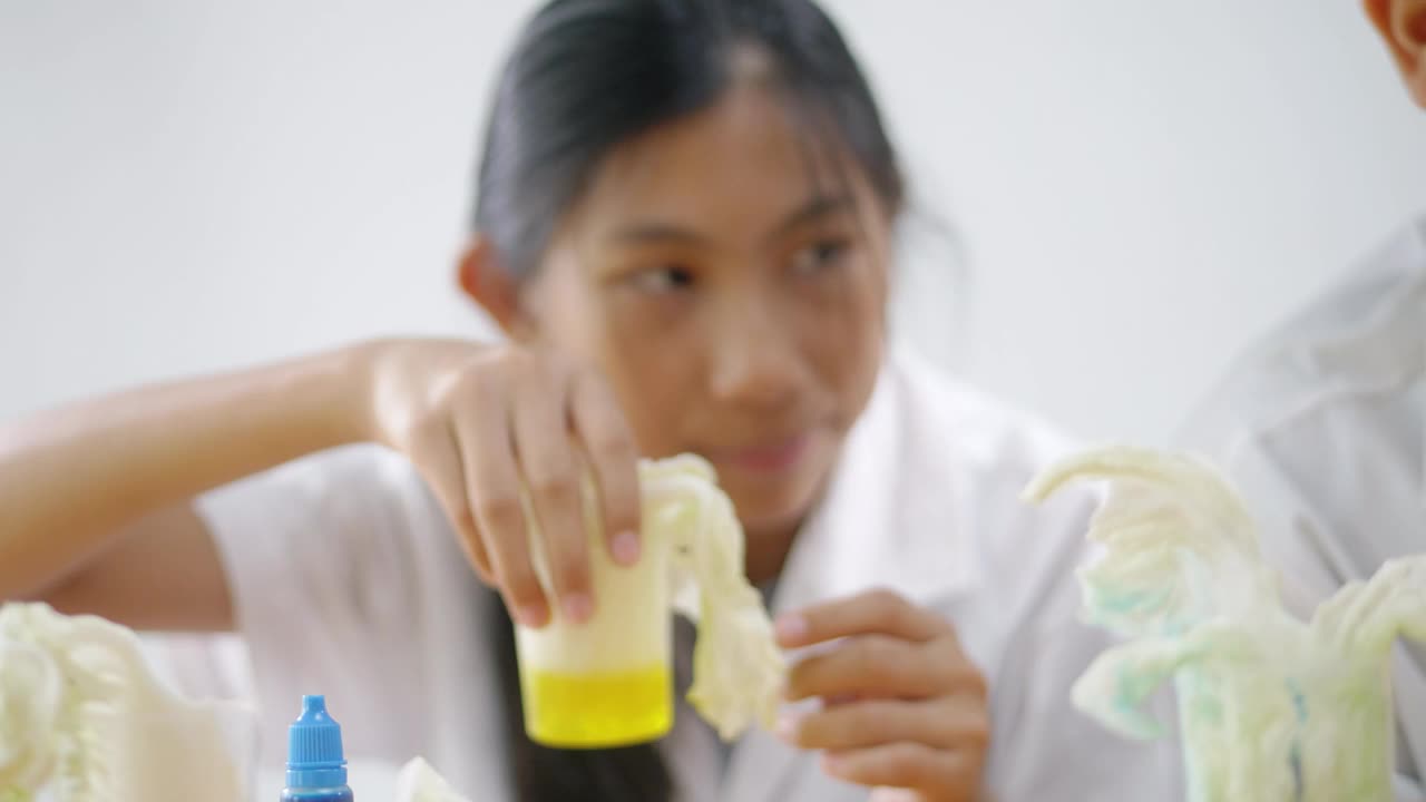 亚洲女孩穿着实验室大褂测试颜色渗透，在家中进行科学实验，教育生活方式理念。视频下载