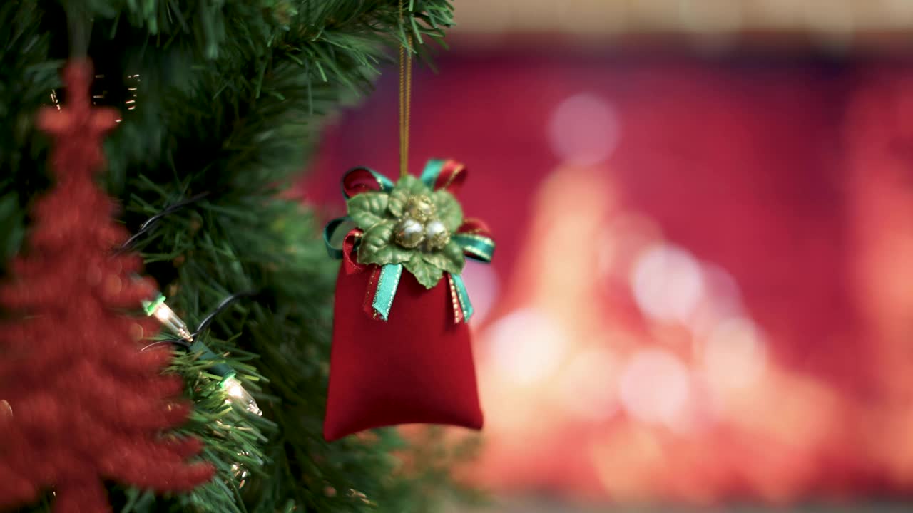 红色装饰袋挂在圣诞树的树枝上，壁炉的火焰模糊的背景和彩色的灯光散景。圣诞装饰的想法和快乐的节日年底的一年。视频素材