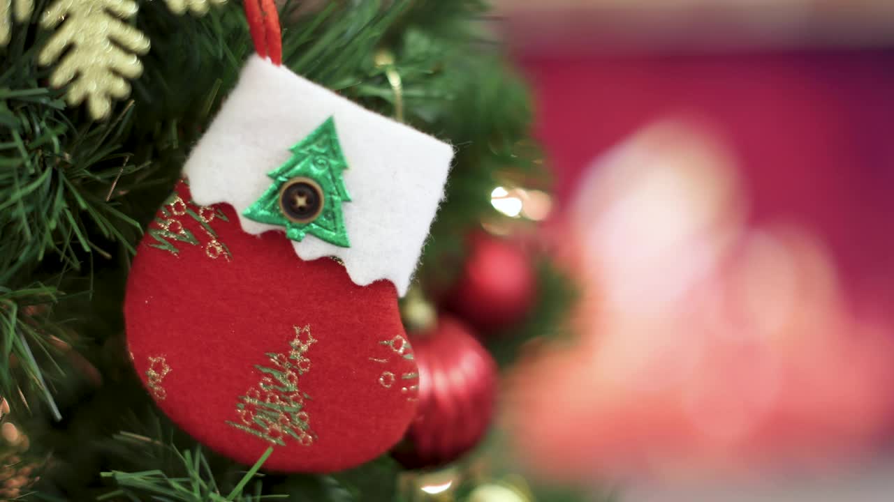 红色装饰装饰袜子挂在圣诞树的树枝上，壁炉的火焰模糊的背景和彩色的灯光散景。圣诞装饰的想法和快乐的节日年底的一年。视频素材