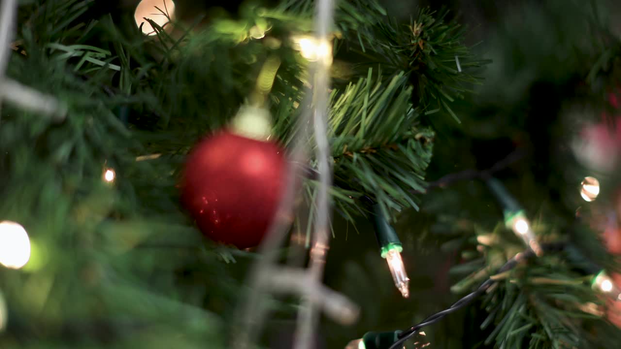 红色装饰球挂在圣诞树的树枝上，壁炉的火焰模糊的背景和彩色的灯光散景。圣诞装饰的想法和快乐的节日年底的一年。视频素材