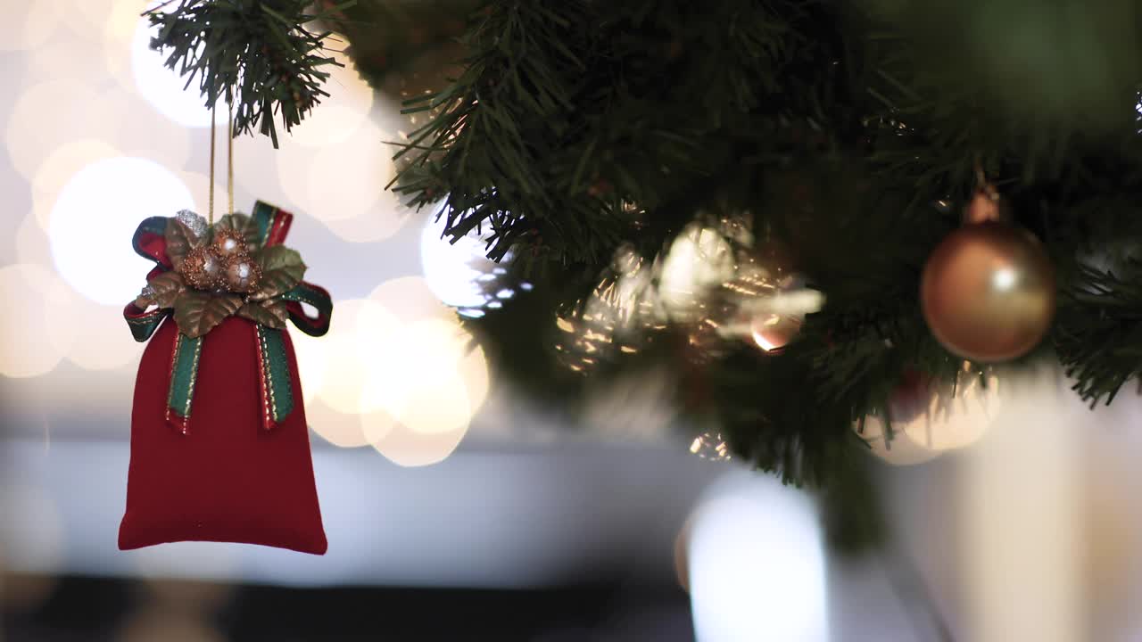红色装饰袋挂在圣诞树的树枝上，壁炉的火焰模糊的背景和彩色的灯光散景。圣诞装饰的想法和快乐的节日年底的一年。视频素材