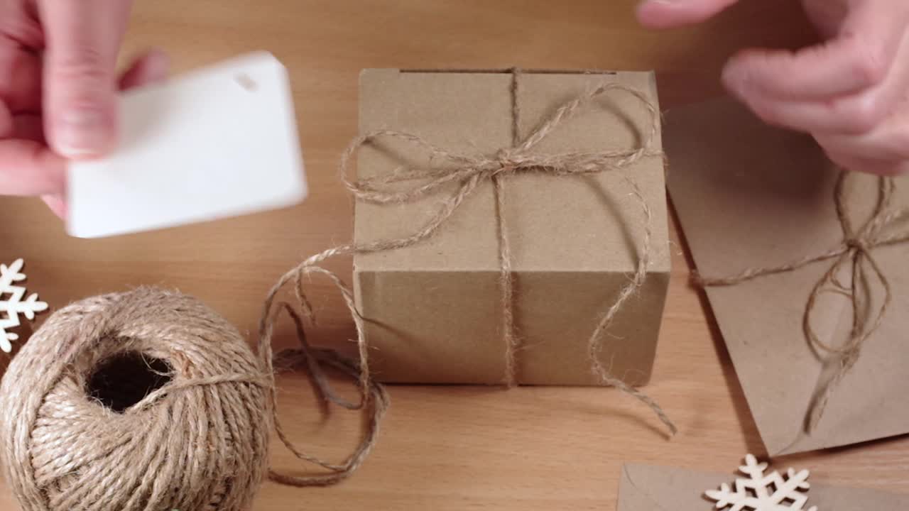 环保礼物，自制礼物，DIY。双手将空白标签贴在一个牛皮纸盒子上，在一张有雪花的桌子上，全高清。“零浪费”的概念视频下载