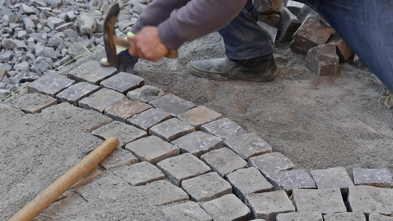建筑工人在道路人行道上安装和铺设石头的特写视频素材