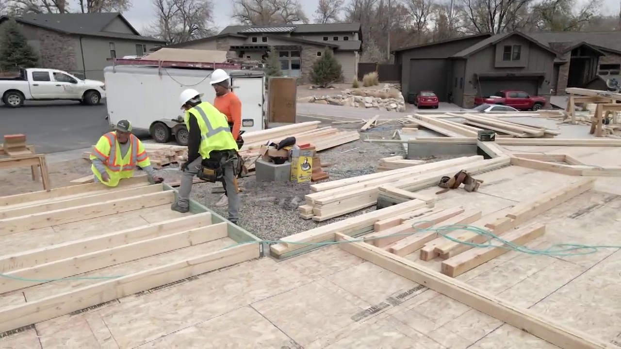 平移多莉拍摄三个人框架人员移动周围的材料和钉在一起的木框架墙被提高在一个新的住宅建筑工地视频素材