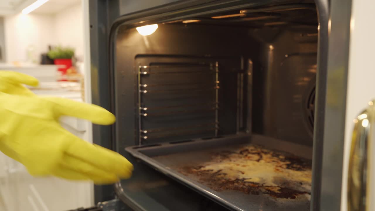 一名妇女在厨房煮完油腻的菜肴后戴着橡胶手套清洗烤箱。清洗烤炉机架前后。视频素材