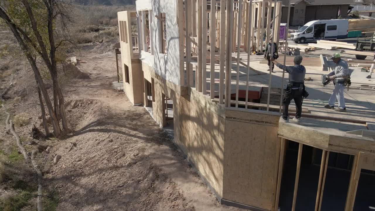 在框架阶段，三名高加索木匠将一面墙滑动到住宅建筑工地的位置视频素材