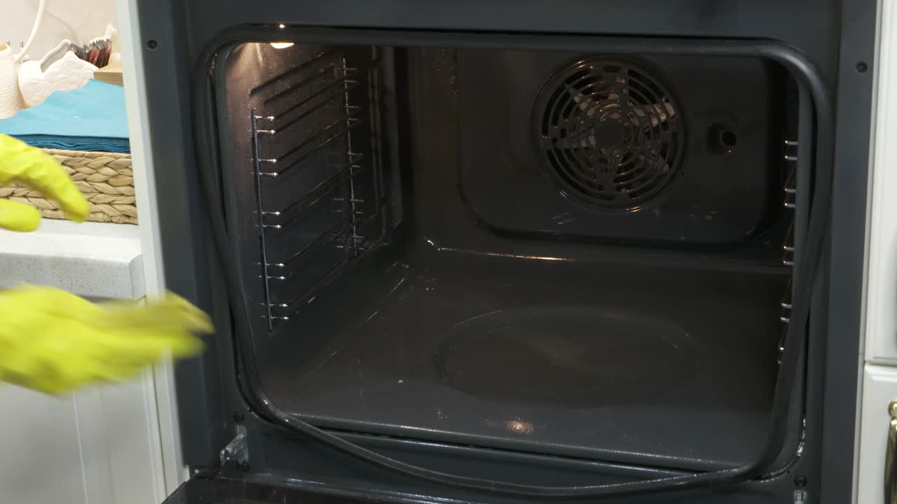 妇女在厨房做饭后戴着橡胶手套清洁烤箱，用布擦拭烤箱。视频下载